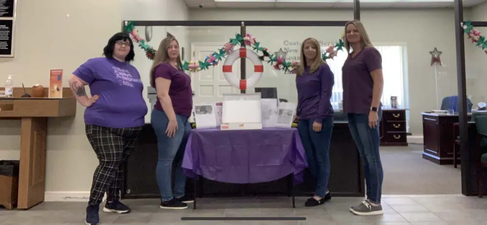 Four women in purple standing at company table posing for photo